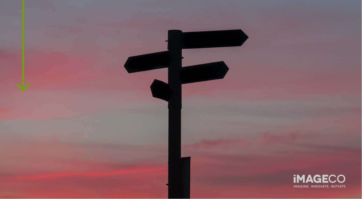 Silhouette of a directions sign against a pink sunset